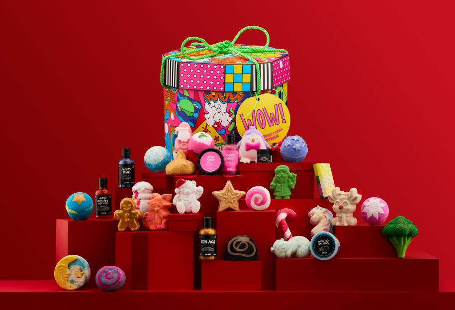 A Lush "WOW!" gift box and various Lush holiday products displayed on red boxes.
