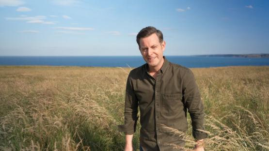 Matt Baker standing in a field near the ocean.