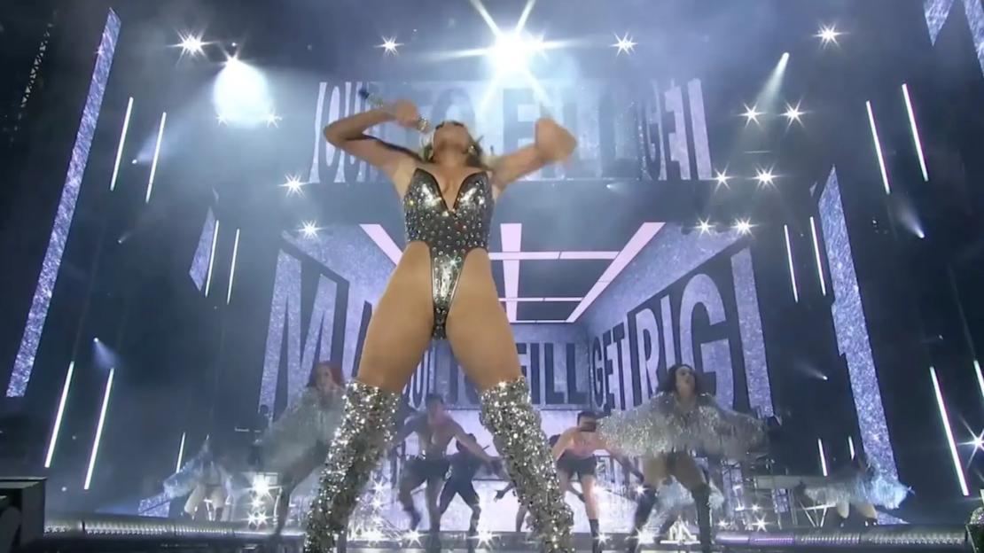 Jennifer Lopez performing on stage in a sparkly bodysuit and boots.