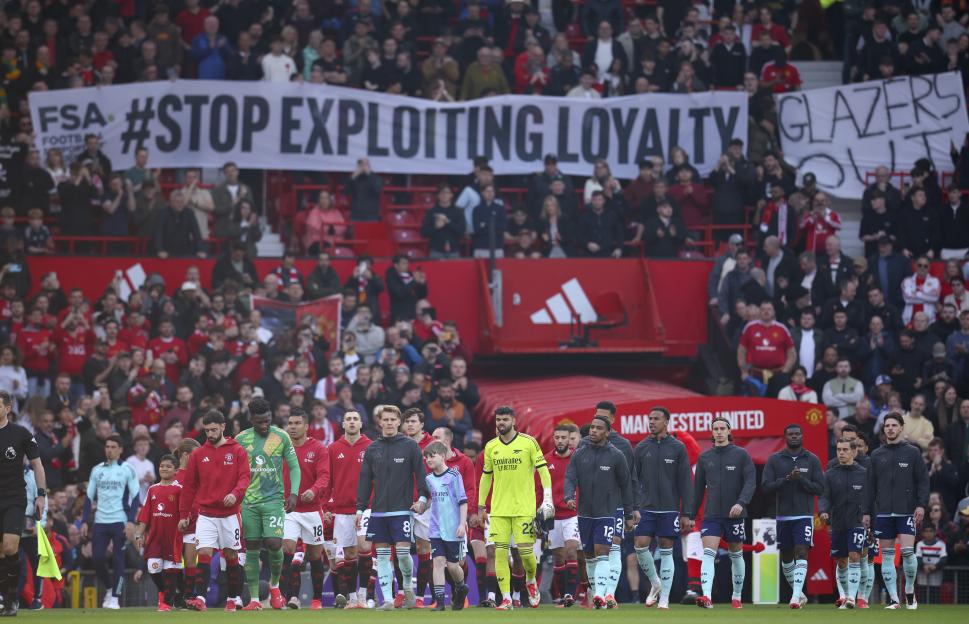 Soccer players walk onto the field past a fan protest banner.