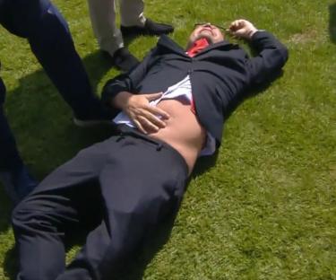 Man lying on the grass, holding his stomach.