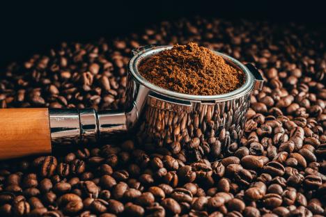 Espresso portafilter filled with ground coffee beans sitting on a bed of coffee beans.