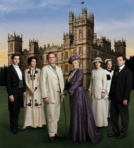 Promotional image for the TV series *Downton Abbey*, featuring the main cast in period costume in front of Highclere Castle.