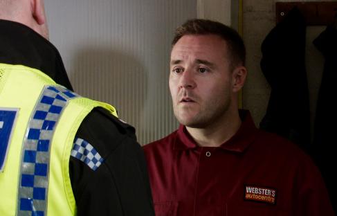 A police officer speaks to a man in a red work shirt.
