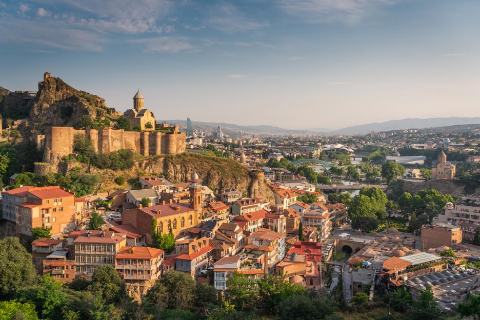 Tbilisi, Georgia cityscape with Narikala Fortress, a church, baths, and homes at sunrise.
