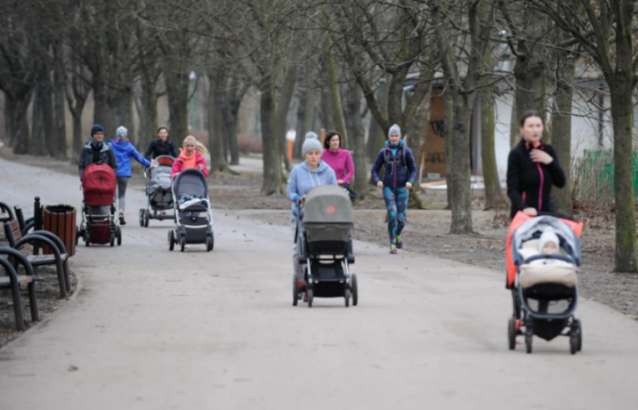 Women pushing strollers on a path in a park.
