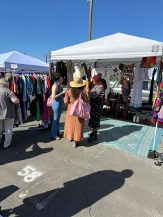 Shoppers browsing clothing at an outdoor market.