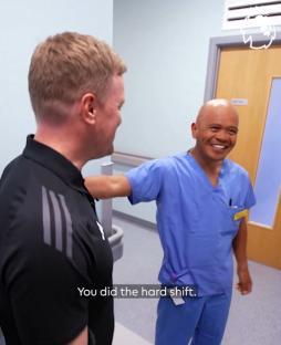 Two men in a hospital hallway; one in scrubs, the other in a polo shirt.