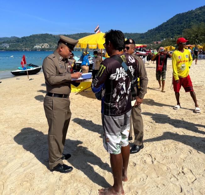 Police officers interviewing a man on a beach.