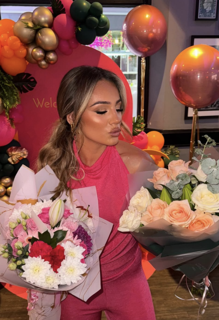 Woman in pink holding two bouquets of flowers.