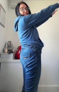 Woman in blue hoodie and jeans, arms outstretched.