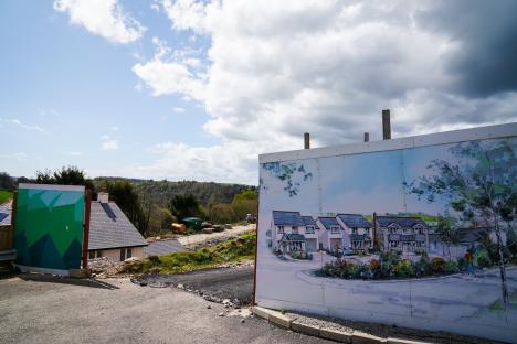 Illustration of a housing development under construction, showing a completed house and a construction hoarding with an artist's rendering of the finished development.