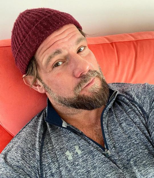 Self-portrait of a man wearing a burgundy beanie and a gray zip-up shirt.