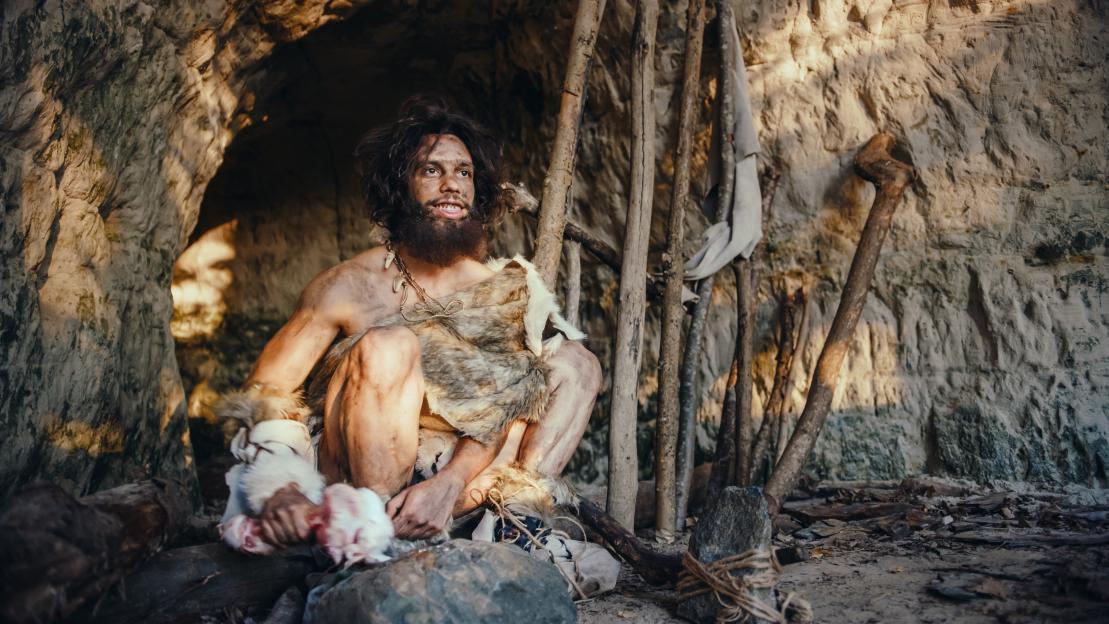 Caveman butchering meat outside his cave.