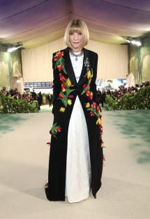 Anna Wintour at the Met Gala in a black coat with floral embroidery over a white dress.
