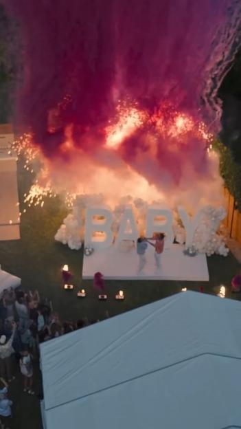 Gender reveal party with pink smoke and "BABY" sign.