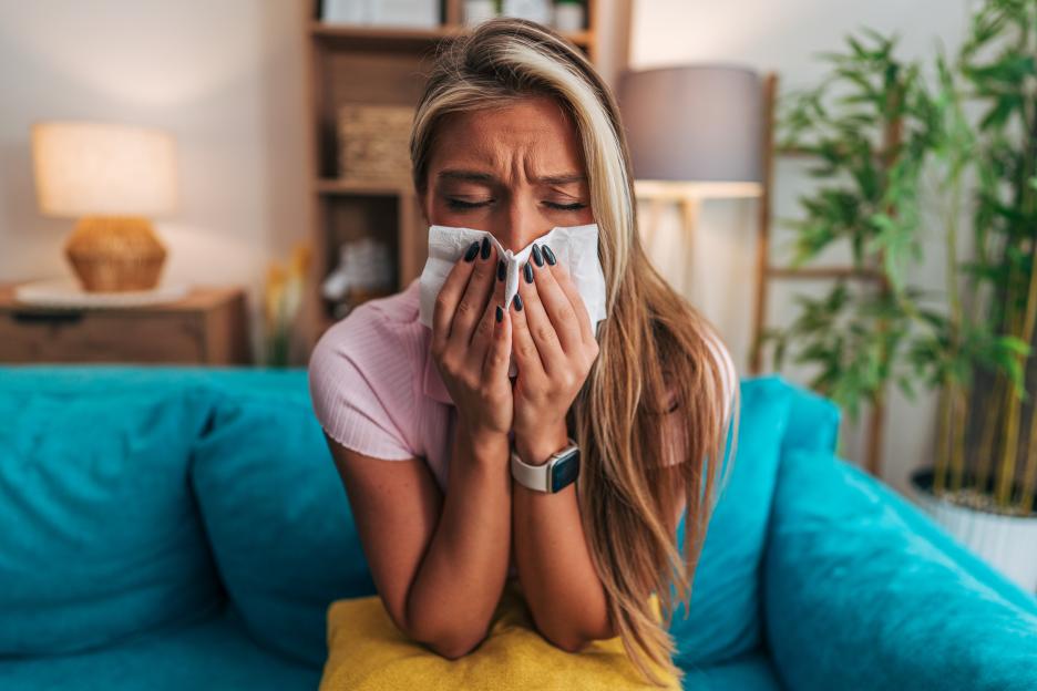 Young woman suffering from a cold, blowing her nose with a tissue.