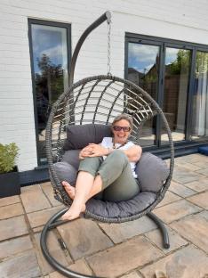 Woman smiling while sitting in a hanging chair on a patio.