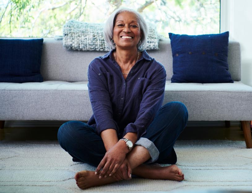 Smiling senior woman sitting cross-legged on the floor in her living room.