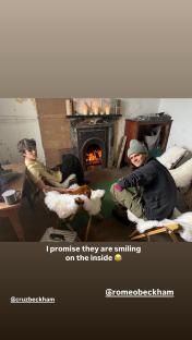 Cruz and Romeo Beckham sitting by a fireplace.