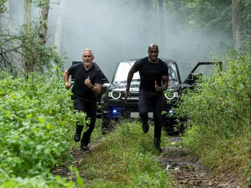 Ground Hunters Karl Beverley and Mel Thomas running on a muddy path with a black SUV in the background.
