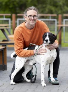 Man kneeling and hugging his black and white dog.