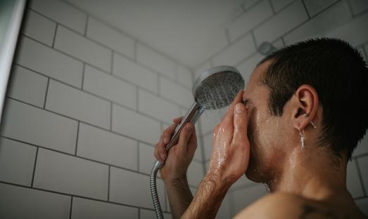 A tattooed man washing his face in a shower.