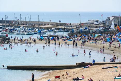 Crowded beach in Lyme Regis, Dorset with people swimming and sunbathing.
