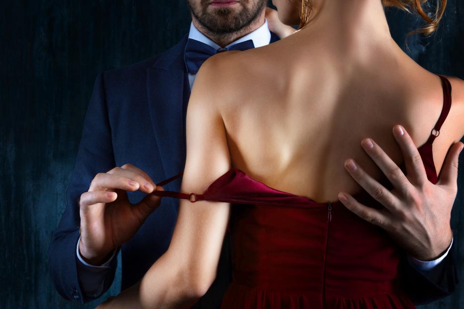 A man in a suit adjusts the strap of a woman's red dress.