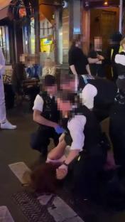 Police officers arresting a person on the ground outside a pub.