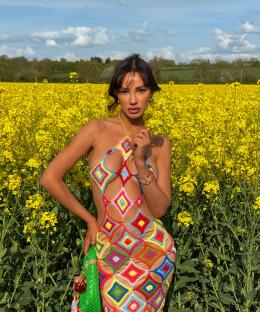 Woman in colorful crochet dress standing in a field of yellow flowers.