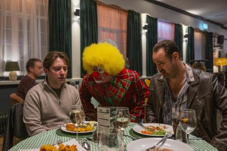 Scene from Mr Bigstuff series two, showing three men at a table, one dressed as a clown.