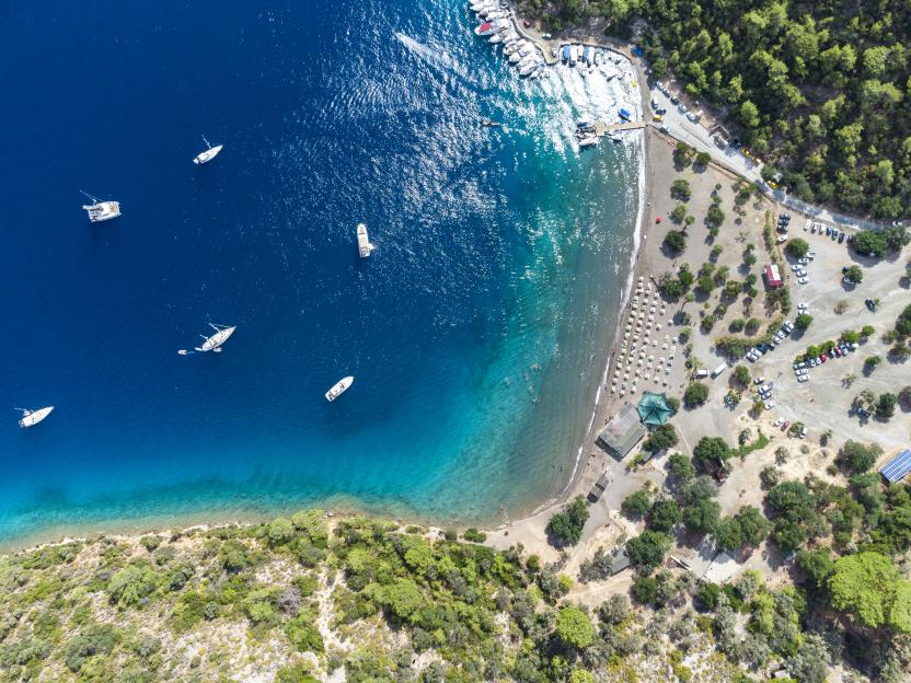 Aerial view of Sarsala Bay, Mugla Dalaman, showing boats in the water and a beach with people.