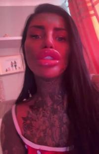 Woman with large lips and tattoos on her neck and chest.