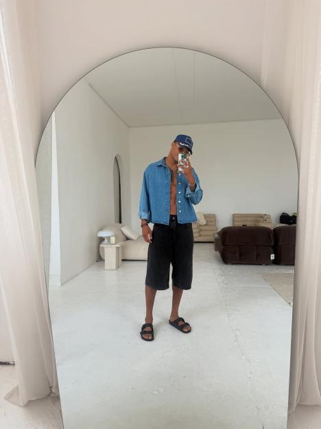 Mirror selfie of a man in a denim shirt and shorts.