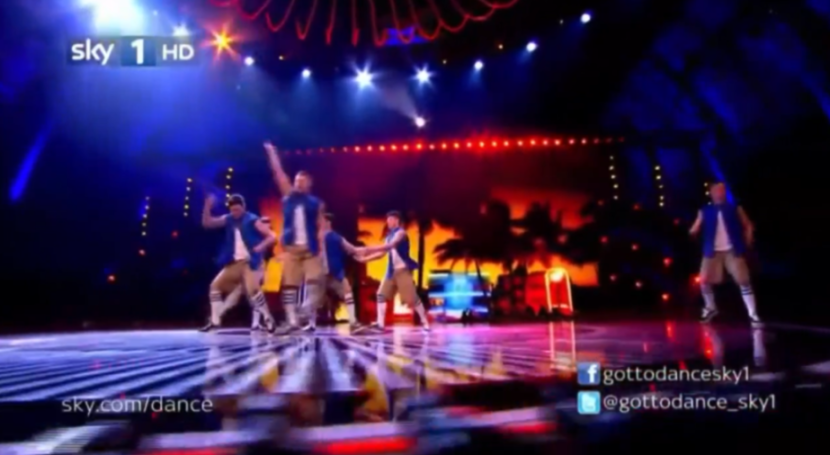 A group of dancers on a stage with a tropical-themed backdrop.