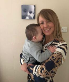 Woman holding baby, with a framed photo of a baby on the wall.