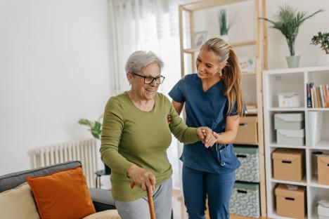 Caregiver assisting elderly woman to walk with a cane.
