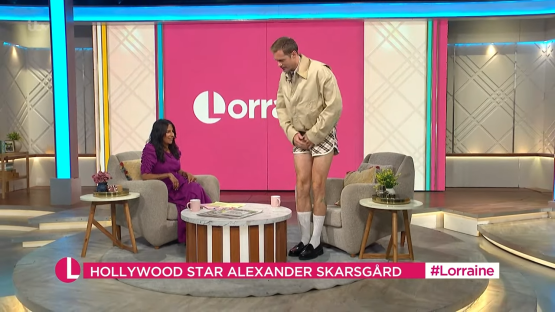 Alexander Skarsgård on a talk show wearing a jacket and shorts.