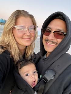 A woman, her ex-husband, her current husband, and their baby on a beach.