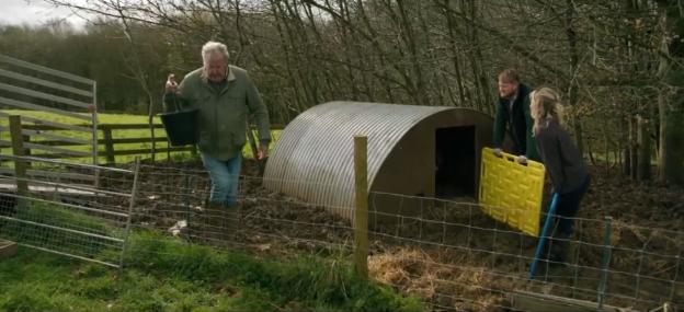 Three people working near a pig shelter on a farm.