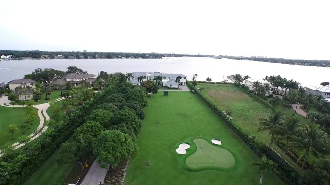 Aerial view of Rickie Fowler's Jupiter Island mansion, with a golf green, large body of water, and surrounding homes.