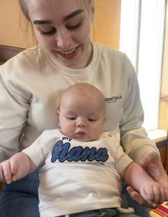 A young woman holding her baby, who is wearing a shirt that says