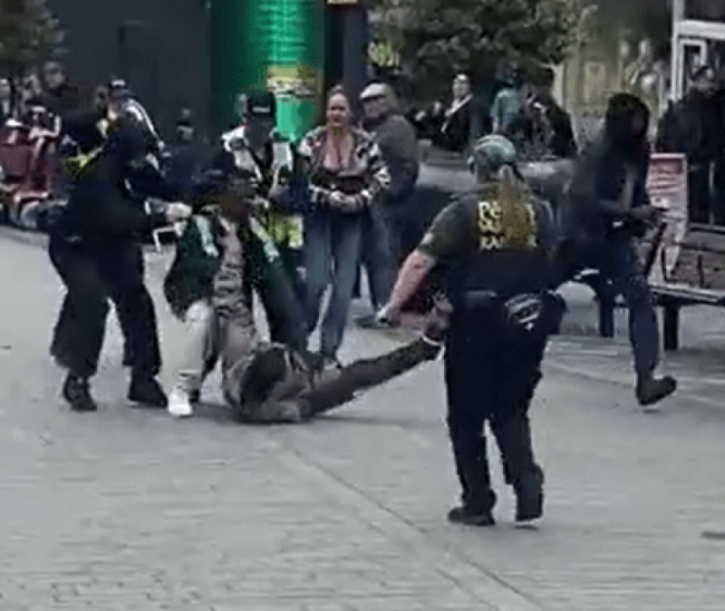 Police officers and a member of the public subduing a man on the ground.