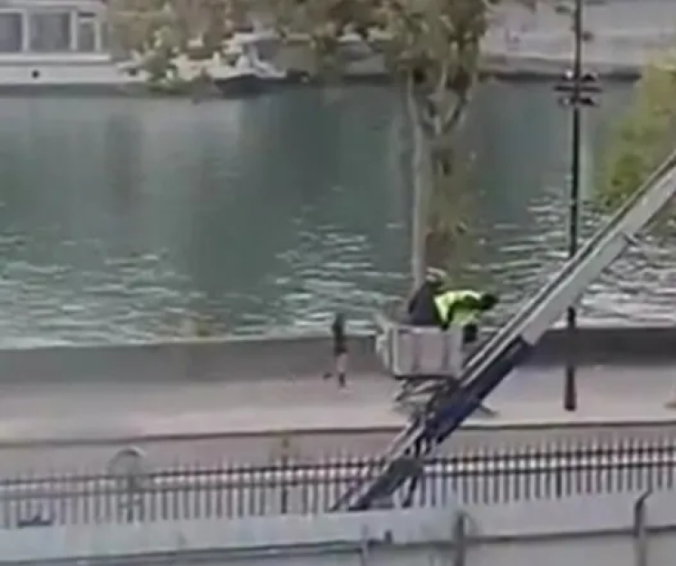 A man in a hi-vis vest operating a cherry picker next to a river.