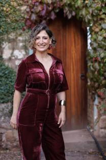 Woman in a burgundy velvet jumpsuit smiling.