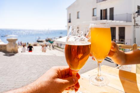 Two people clinking beer glasses at an outdoor cafe.