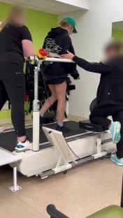 Woman undergoing physical therapy on a treadmill with assistance from two therapists.