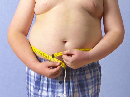 Overweight child measuring waist with tape measure.