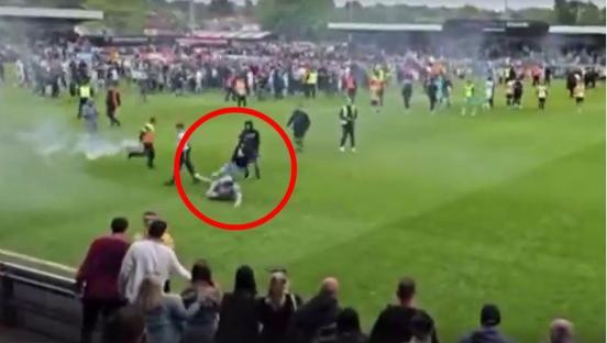 A person being tackled on a soccer field amidst smoke and a large crowd.